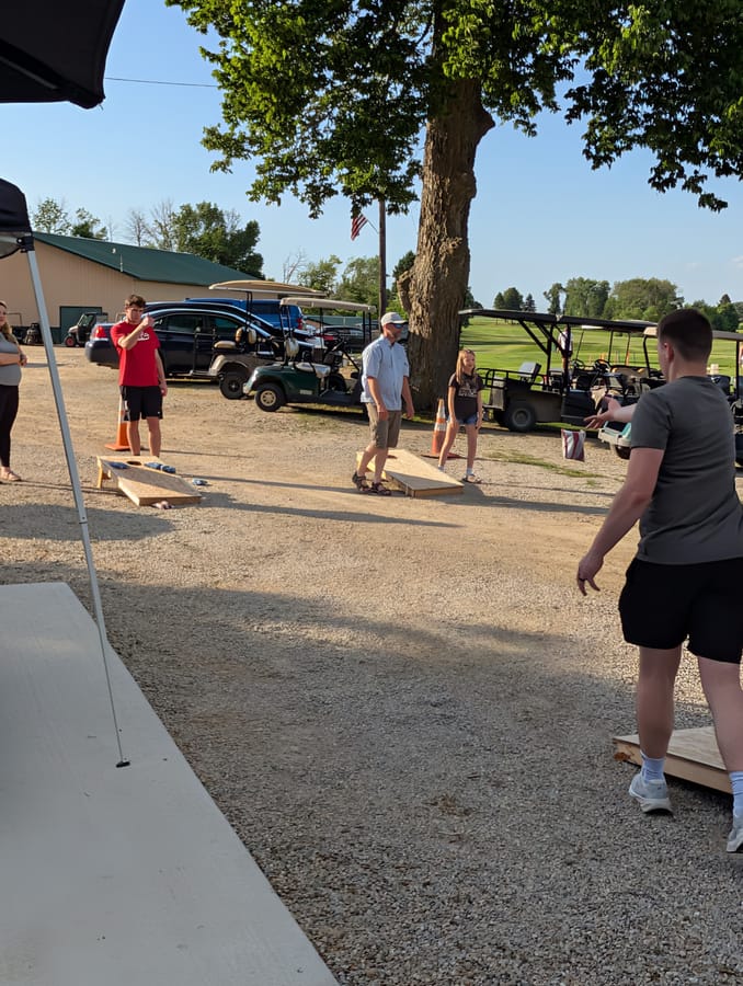 Group playing cornhole outdoors at dusk during a corporate event