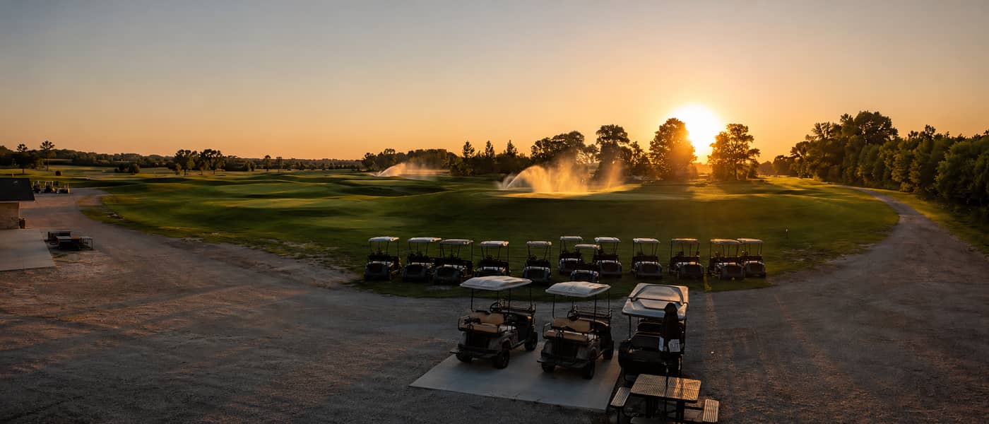 Golf carts lined up on the course at sunset with sprinklers running